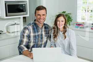 Portrait of smiling couple using laptop in living room at home