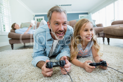 Happy father and daughter playing video game while lying on floor in living room