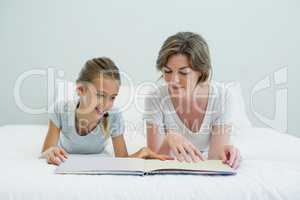 Mother and daughter lying on bed and reading book