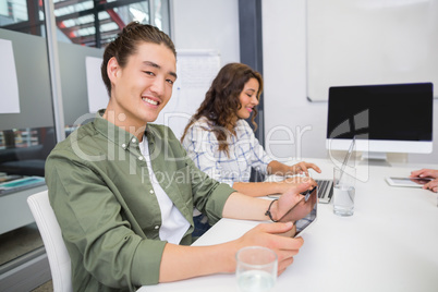 Smiling executive using laptop and digital tablet in conference room