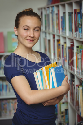 Portrait of schoolgirl standing with stack of books in library