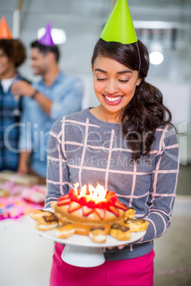 Happy female executive wearing party hat and holding birthday cake