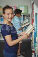 Smiling schoolgirl reading book in library at school
