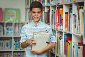 Portrait of schoolboy holding books in library