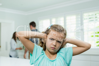Girl covers her ears with her hands while parents arguing in background