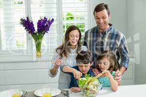 Smiling family preparing bowl of salad in kitchen