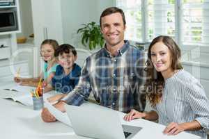 Smiling parents working with laptop and childrens studying in living room at home