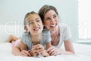 Smiling mother embracing her daughter while lying on bed in bedroom