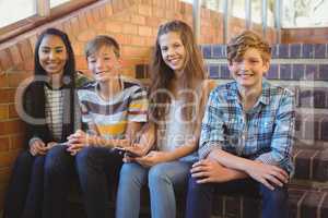 Smiling school students sitting on the staircase using mobile phone