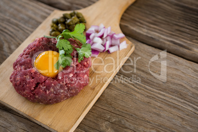 Minced meat with egg yolk, onions and olives on wooden tray