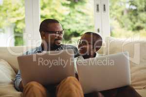 Father and son sitting on sofa and using laptop