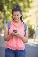 Smiling school girl with schoolbag using mobile phone in campus