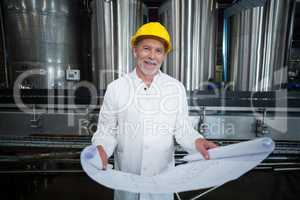 Smiling factory engineer standing in bottle factory with blueprint