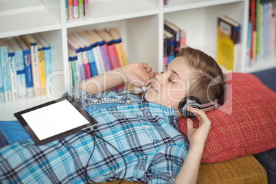 Schoolboy relaxing on couch while listening music on digital tablet in library