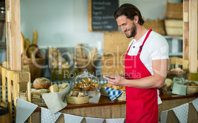 Smiling bakery staff using mobile phone at counter