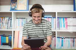 Happy schoolboy listening music while using digital tablet in library