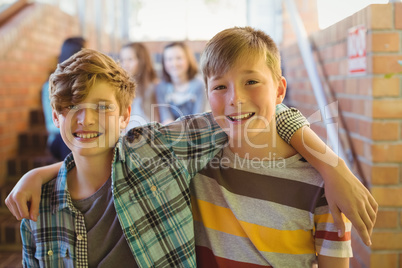 Portrait of smiling schoolboys standing with arm around in corridor