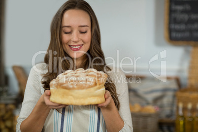 Smiling female staff holding round loaf of bread at counter