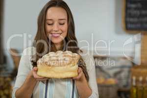 Smiling female staff holding round loaf of bread at counter