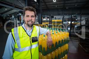 Portrait of factory worker leaning on packed orange juice bottles crate