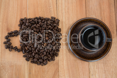 Cup of black coffee and coffee beans forming shape of cup