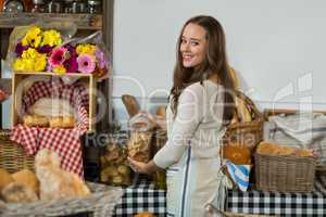 Portrait of smiling female staff holding a jar of cookies at counter