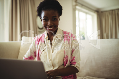 Portrait of woman sitting on sofa and using laptop in living room