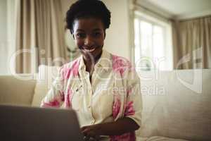 Portrait of woman sitting on sofa and using laptop in living room