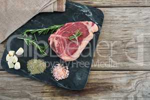 Sirloin chop and ingredients on slate board against wooden background