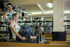 Female trainer assisting woman with stretching exercise on reformer