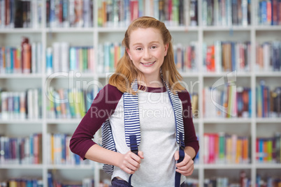 Portrait of schoolgirl standing with schoolbag in library