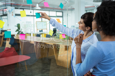 Female graphic designer pointing to the sticky notes on the glass in creative office