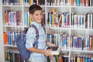 Happy schoolboy selecting books in library