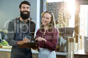 Portrait of smiling bakery staff writing on clipboard at counter