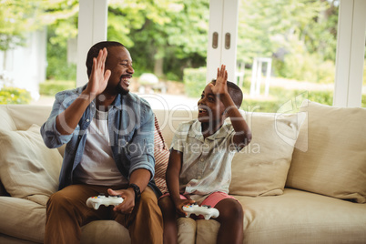 Father and son giving high five to each other while playing video game