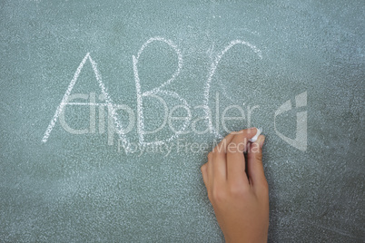 Hand of schoolgirl writing on chalkboard in classroom