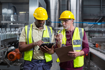 Two factory workers with clipboard and digital tablet working in the plant