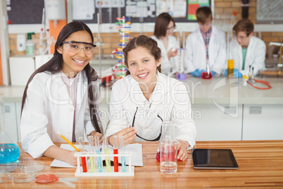 School girls writing in journal book while experimenting in laboratory at school