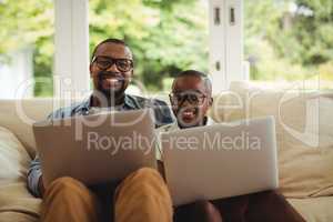 Father and son sitting on sofa and using laptop