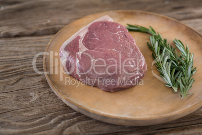 Sirloin chop and rosemary on wooden tray against wooden background