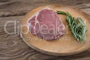 Sirloin chop and rosemary on wooden tray against wooden background