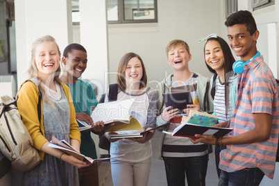 Group of smiling students standing with notebook in corridor