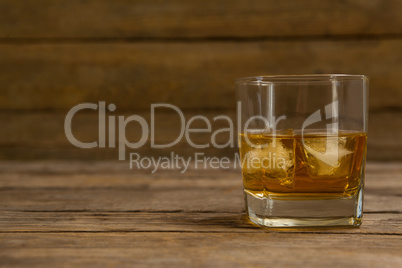 Glass of whisky with ice cube on wooden table