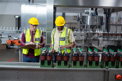 Two factory workers monitoring cold drink bottles in the plant