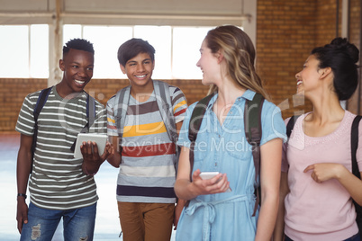 Happy students interacting while using mobile phone and digital tablet in campus