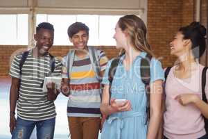 Happy students interacting while using mobile phone and digital tablet in campus