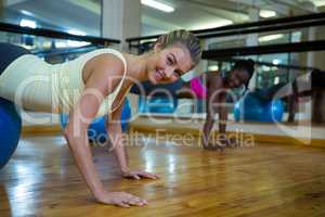 Smiling woman doing pilates exercises on fitness ball with coach in fitness studio