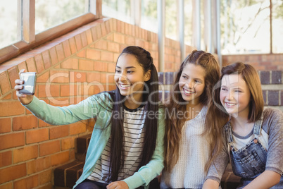 Smiling schoolgirls sitting on the staircase taking selfie with mobile phone