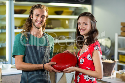 Portrait of salesman and costumer holding gouda cheese at counter