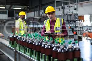 Factory worker with digital tablet monitoring drinks production line